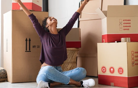 Young woman sitting amongst moving boxes and celebrating