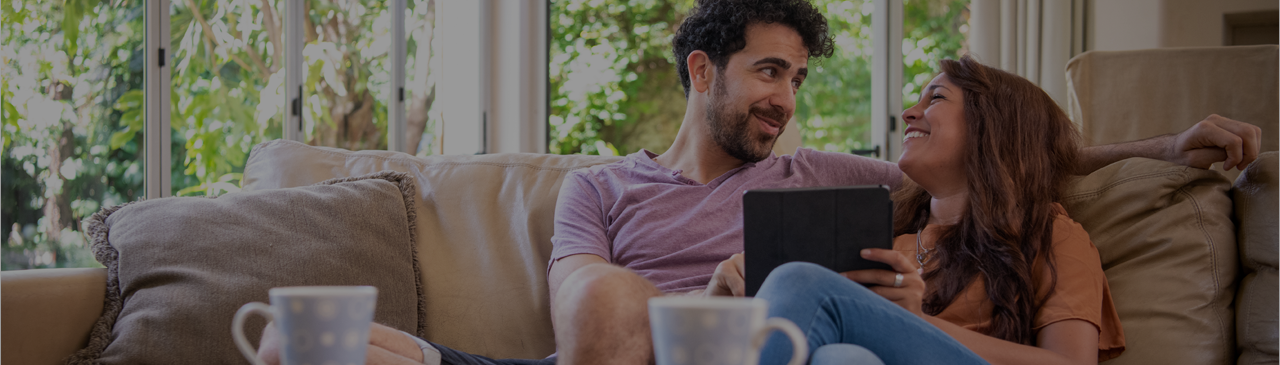 Couple on Couch Smiling at Each Other While Browsing FirstOntario Personal Products on Tablet