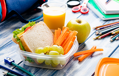 Lunch in Tupperware on Table with Orange Juice and School Supplies