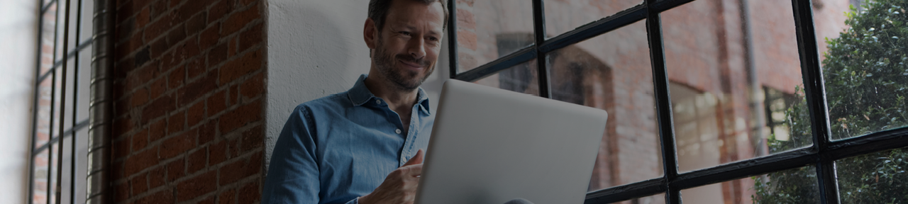 Man Smiling While Viewing FirstOntario Annual Reports on Laptop