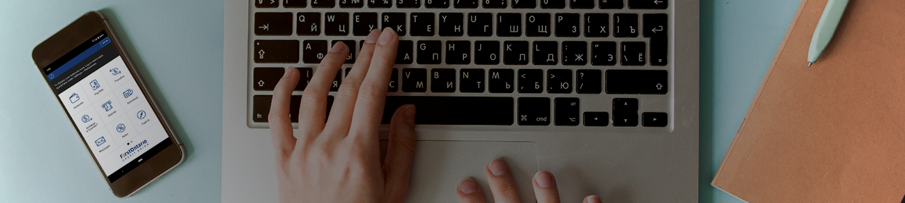 Person Typing on Laptop with FirstOntario Mobile App Open on Phone