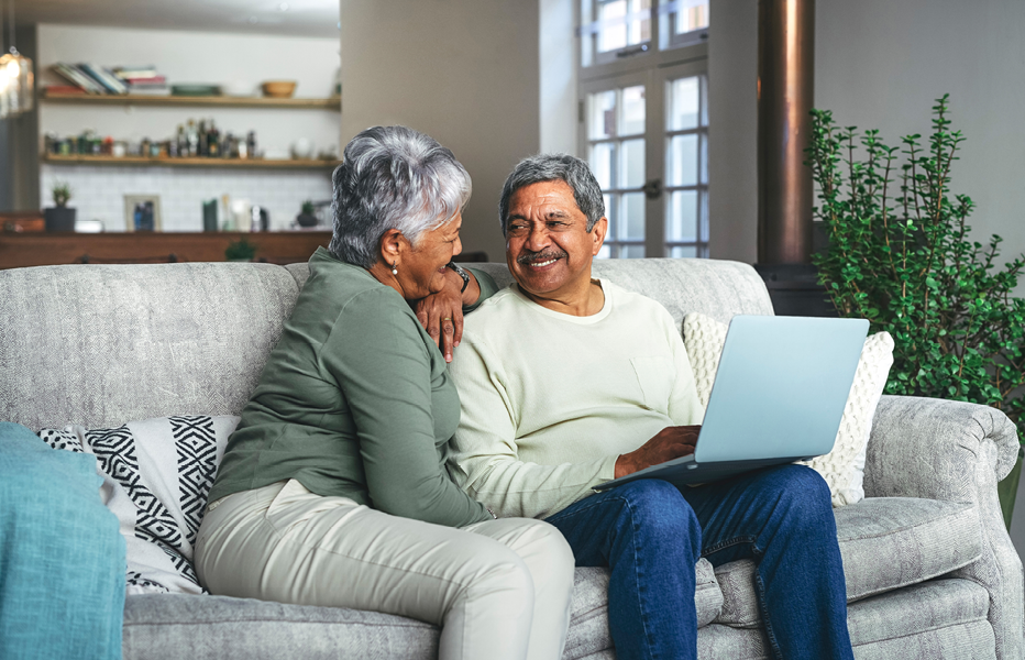 Couple Smiling at Each Other While Using Laptop on Couch