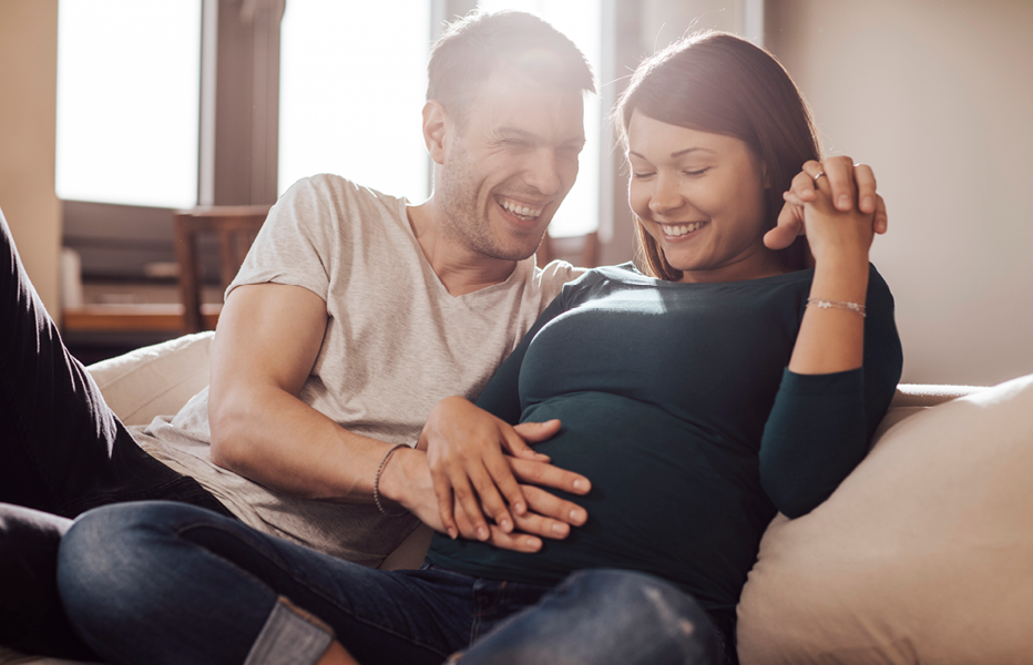 Pregnant Couple Sitting on Couch Holding Baby in Belly