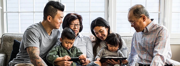 Three generations of family sitting together on a couch while looking at tablet