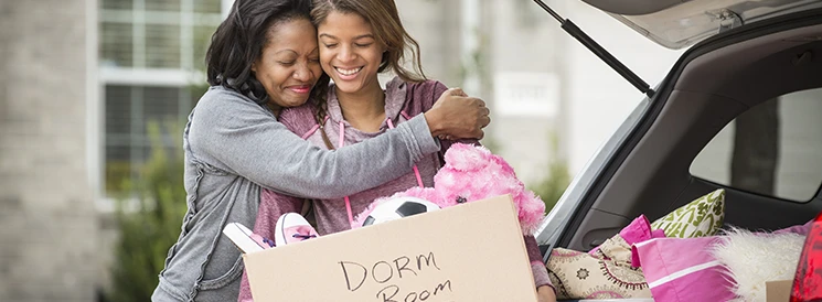 Mother and daughter hugging while loading dorm room moving boxes into car 