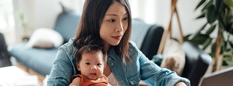 Woman holding baby while planning TFSA contribution investments on laptop