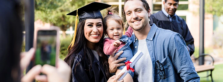 Graduate with diploma posing for picture with husband and child
