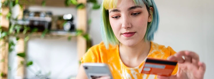 Young woman with colourful hair logging into mobile banking with debit card