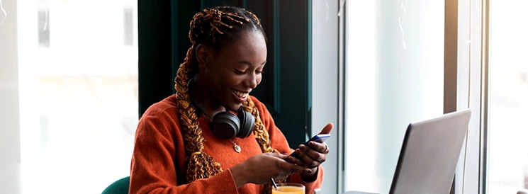 Woman smiling while using phone and laptop at a coffee shop