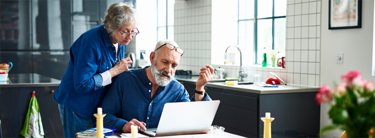 Elderly couple reviewing tax return on laptop in kitchen