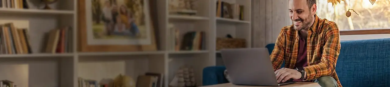 Man in orange shirt smiling while using laptop