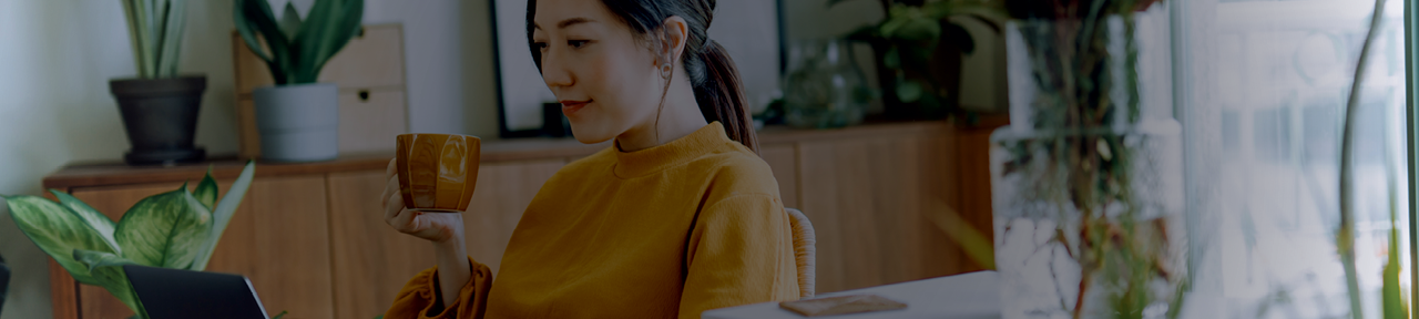 Woman Drinking Coffee and Browsing Chequing Accounts on Laptop