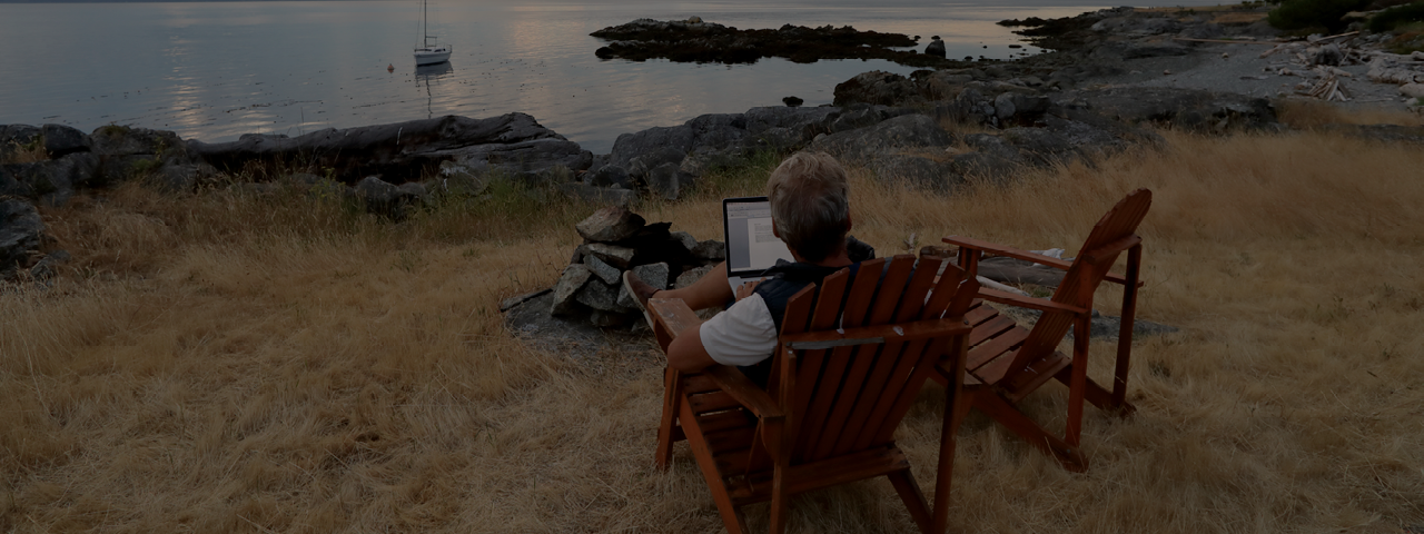 Person with Laptop Sitting on Muskoka Chair by the Water