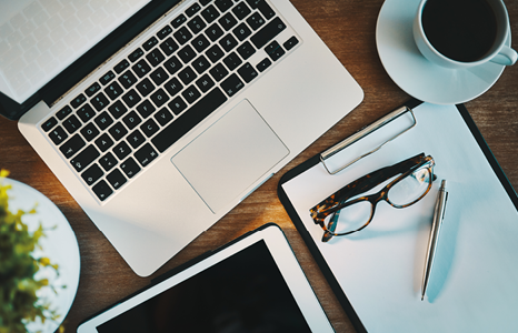 Desk with Laptop, Tablet, Notebook, Glasses and Coffee Cup