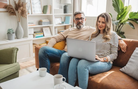 Couple sitting on a couch reviewing financial goals on laptop