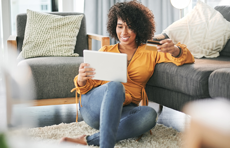 Woman sitting on floor in home holding tablet and FirstOntario Visa credit card