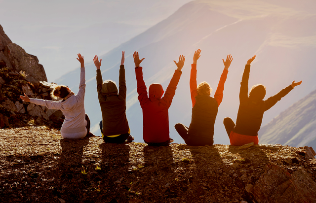 Group of People Sitting on Cliff with Hands in the Air
