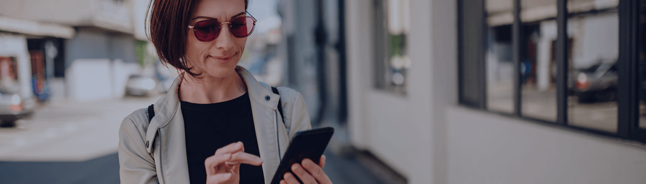 Woman Wearing Sunglasses Walking Down Street Holding Mobile Phone