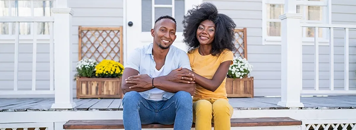 Smiling couple sitting on front porch with potted plants