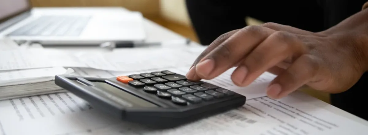 Person Typing on Calculator with Papers on Desk