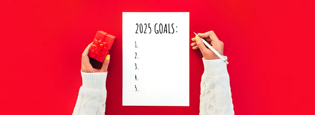 Person holding pen and red present jotting down 2025 goals