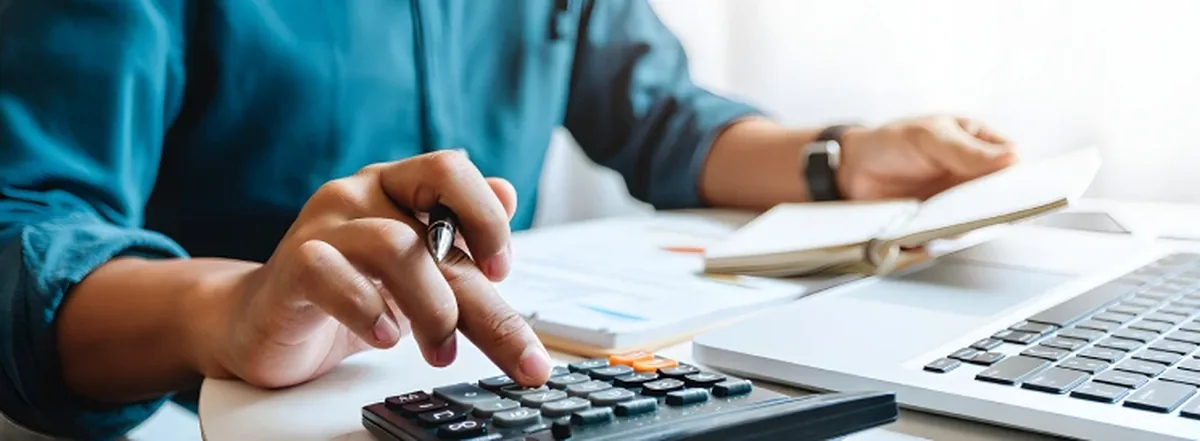 Person using calculator at desk with laptop