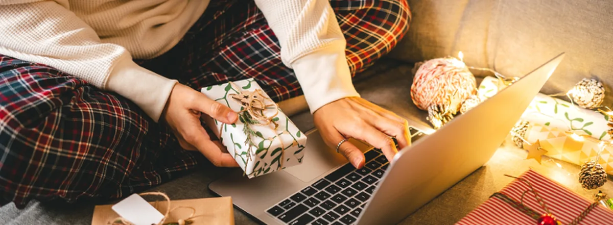 Person wrapping holiday presents while using laptop