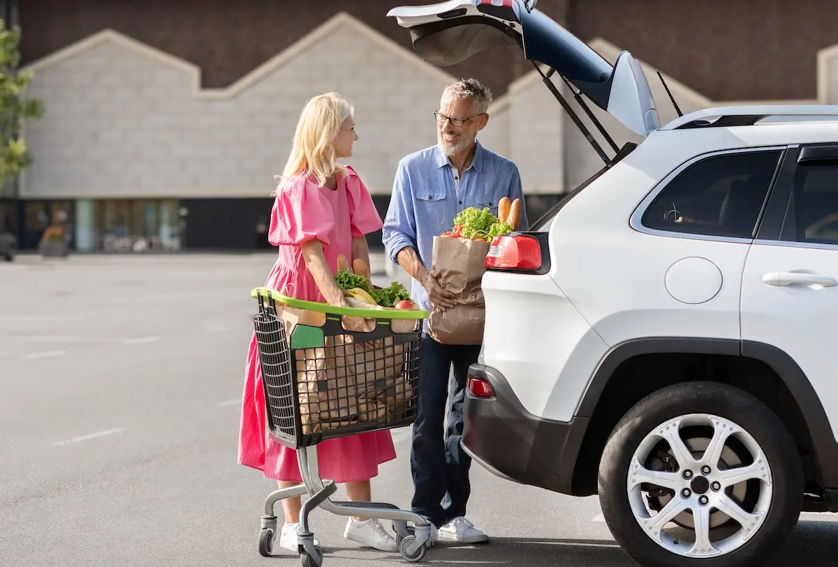 A mature couple loading groceries into the trunk of their SUV in a parking lot, smiling and enjoying a stress-free shopping trip.