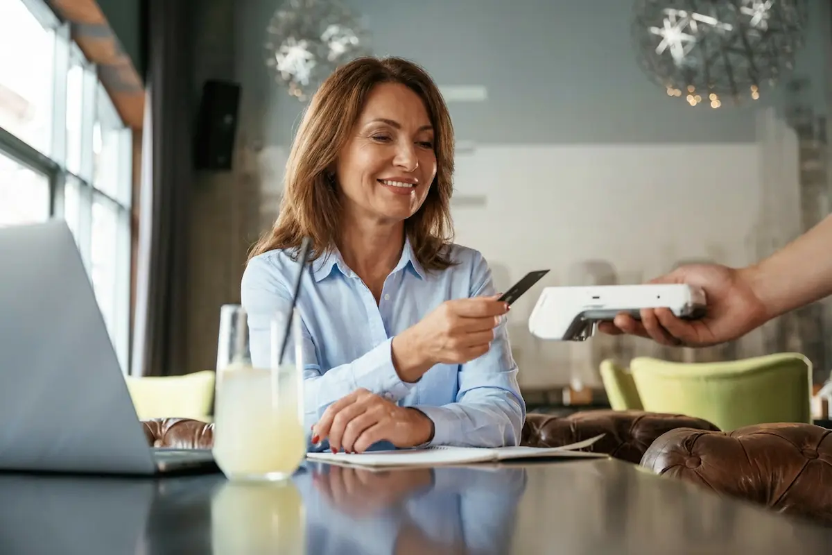 A smiling woman in a cafe using a debit card to pay via a contactless terminal.
