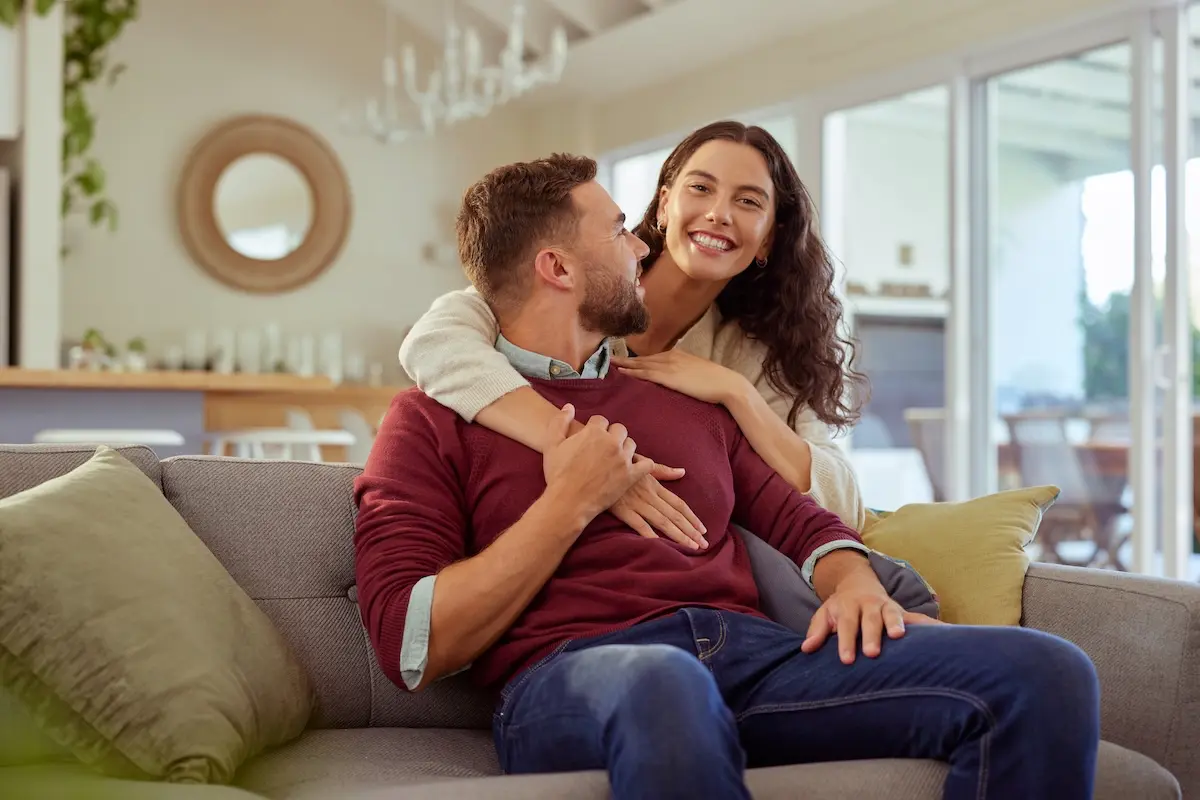 Smiling couple sitting together on a sofa at home, enjoying a comfortable and secure lifestyle.