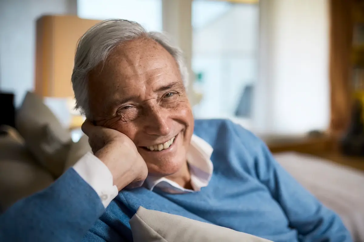 Man in bue sweater smiling and relaxing on the couch.