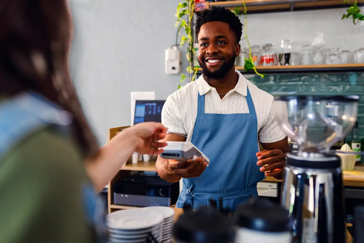 Barista accepting a FirstOntario contactless credit card payment from a customer at a café counter.