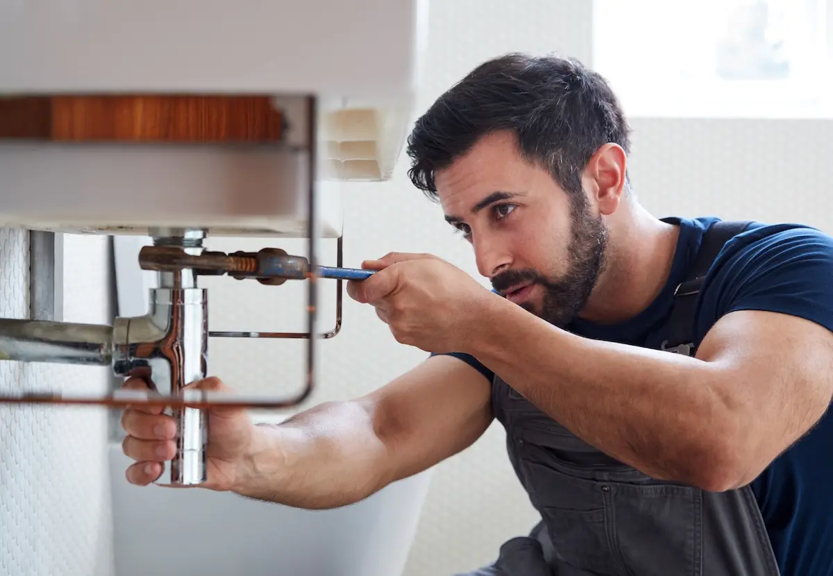 Plumber fixing a sink under a bathroom vanity.
