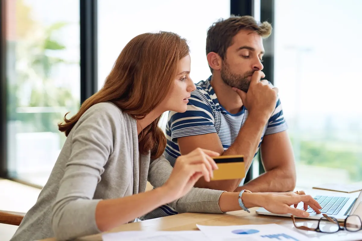 Couple reviewing their finances online and using a credit card while planning debt consolidation and loan repayment at home.