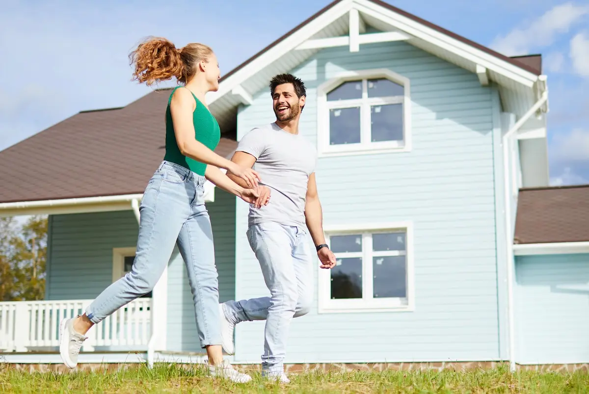 A joyful couple running in front of their blue Ontario home, celebrating the financial flexibility provided by their MeritLine Home Equity Line of Credit.