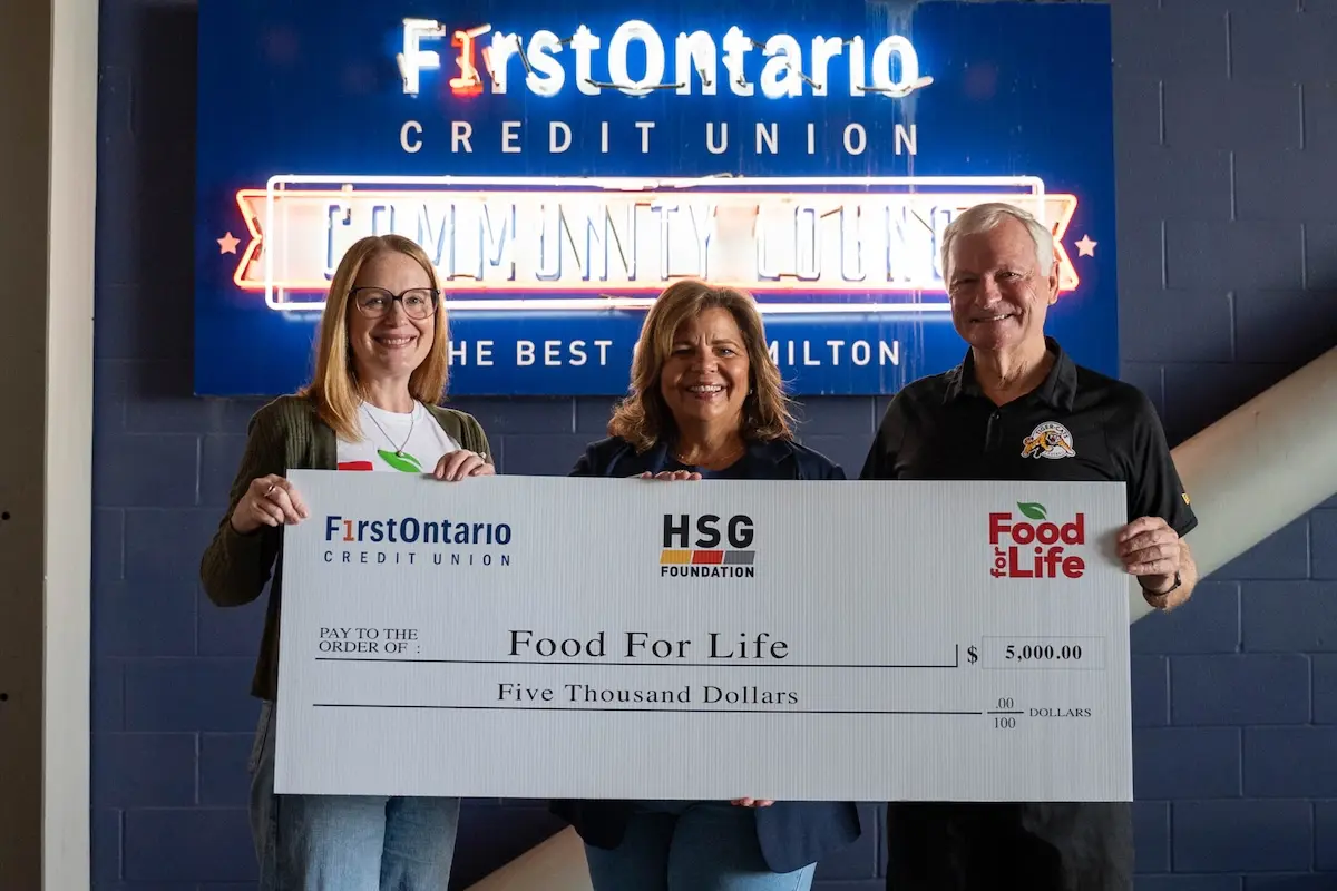 Three people smile and hold a large ceremonial cheque.