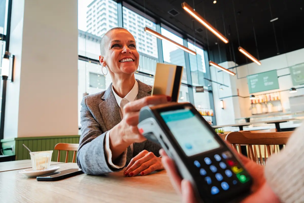 Mid-adult woman paying the bill with a contactless business debit card in a restaurant.