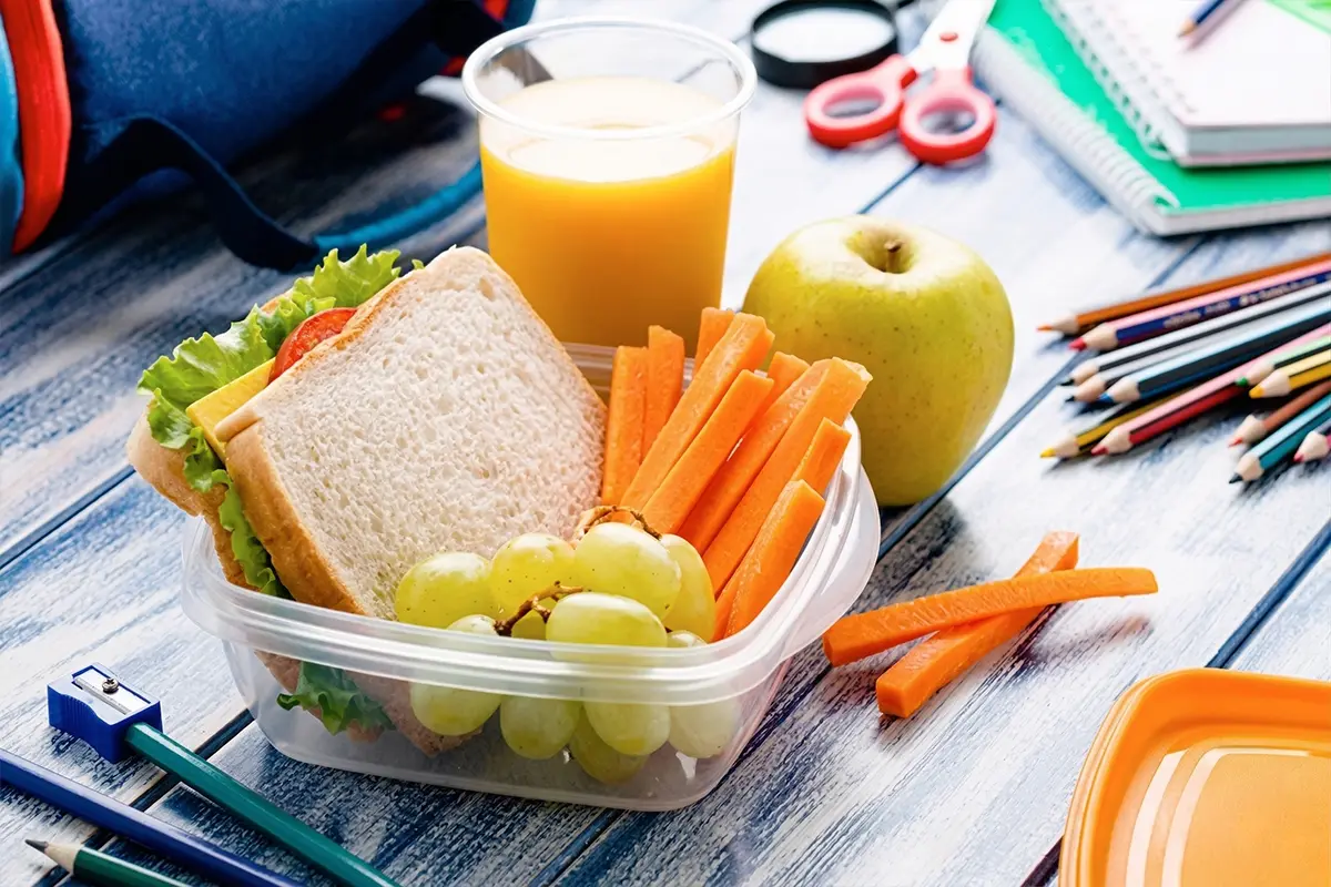 Lunch in Tupperware on Table with Orange Juice and School Supplies.