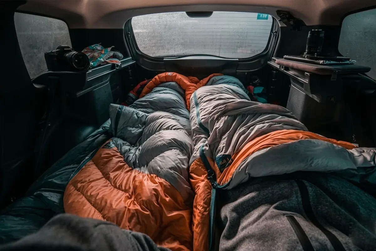 Two People Sleeping in Sleeping Bags in Back Seat of Car
