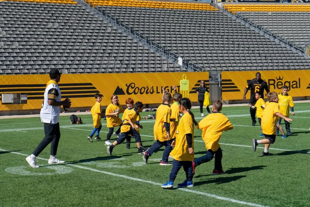 Kids in yellow shirts playing football with Hamilton Tiger Cats players.