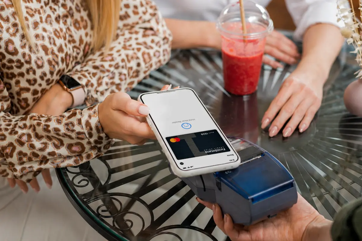 A customer makes a contactless payment at a café by holding a smartphone over a card reader.