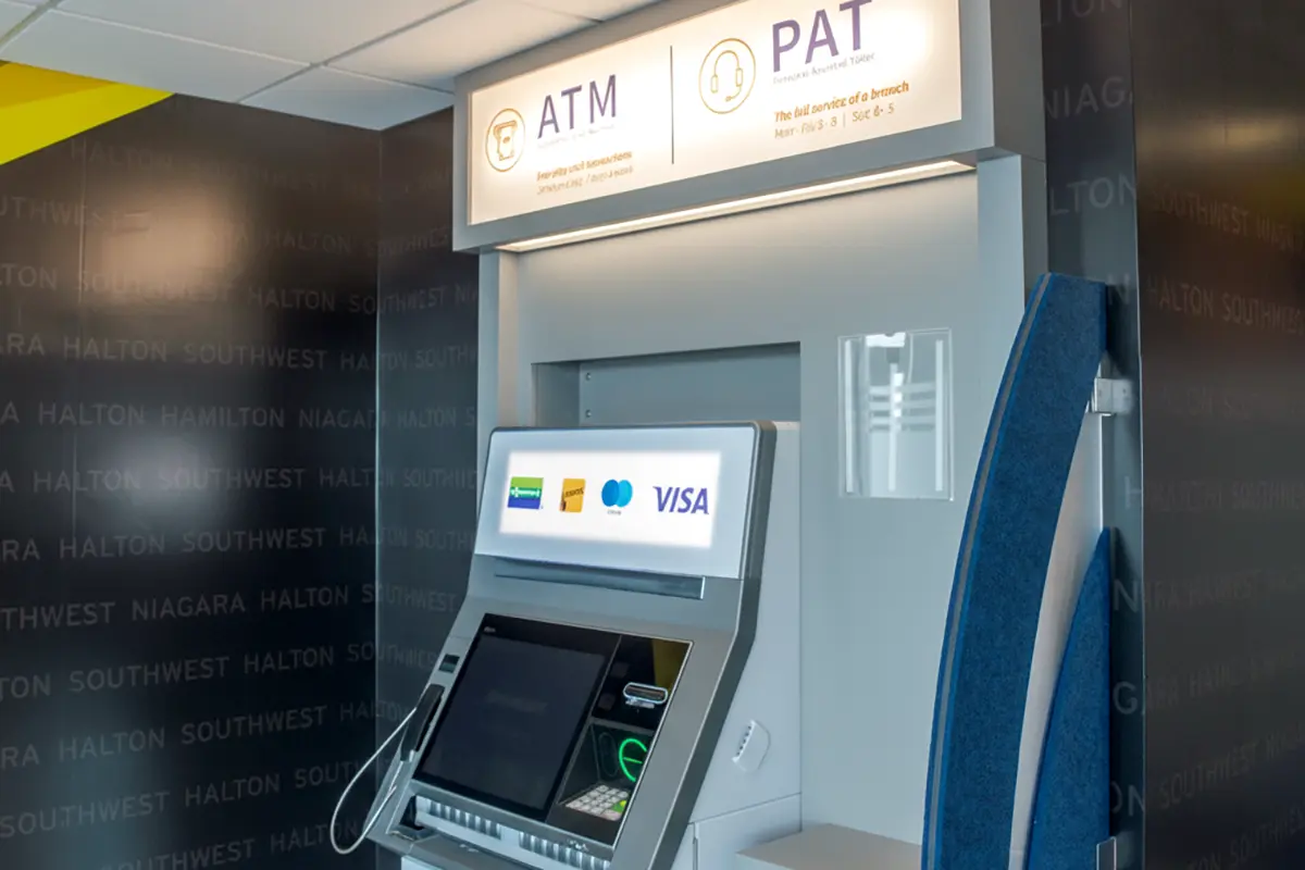 Indoor ATM machine with a screen displaying card options including Visa, Interac, and THE EXCHANGE Network, located beneath signage for ATM and PAT services in a modern banking area.