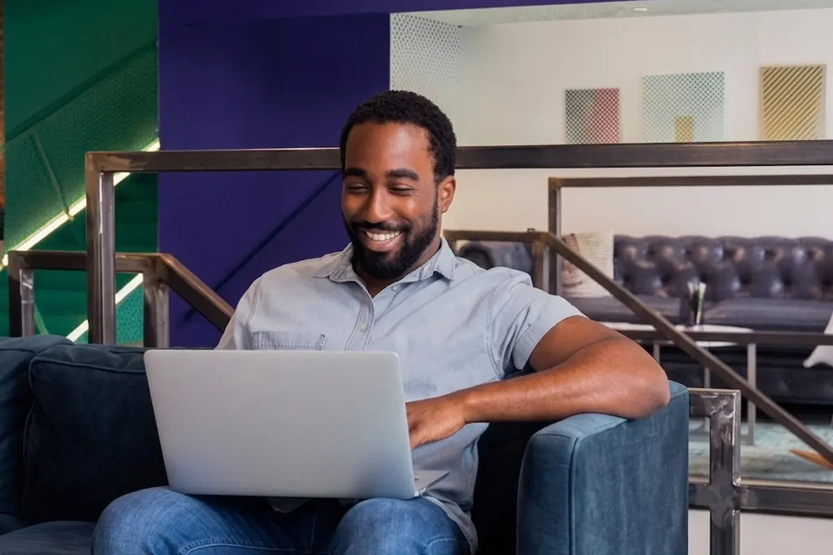Business owner smiling while using a laptop in a modern office, managing operations online.