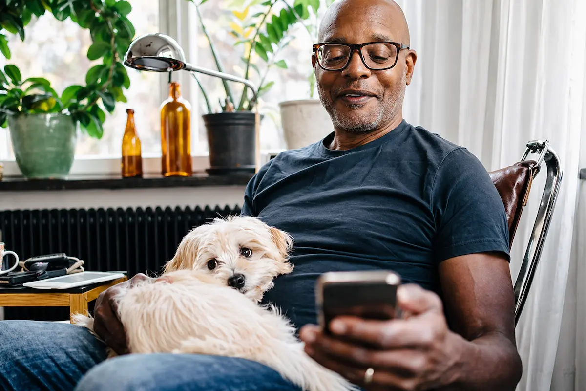Man relaxing at home with a small dog while checking his smartphone.