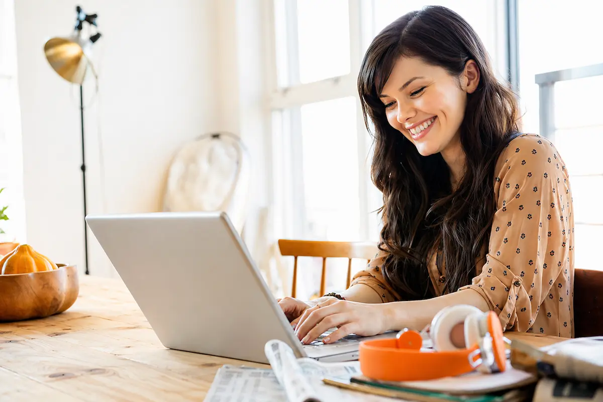 Woman smiling while using a laptop at home, representing safe and convenient online banking.