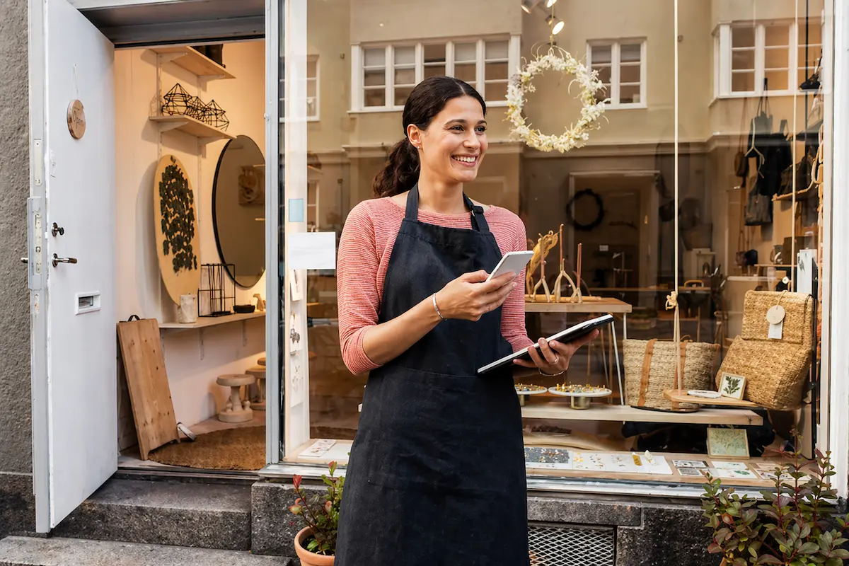 Smiling Shop Owner Standing Outside Storefront with Phone