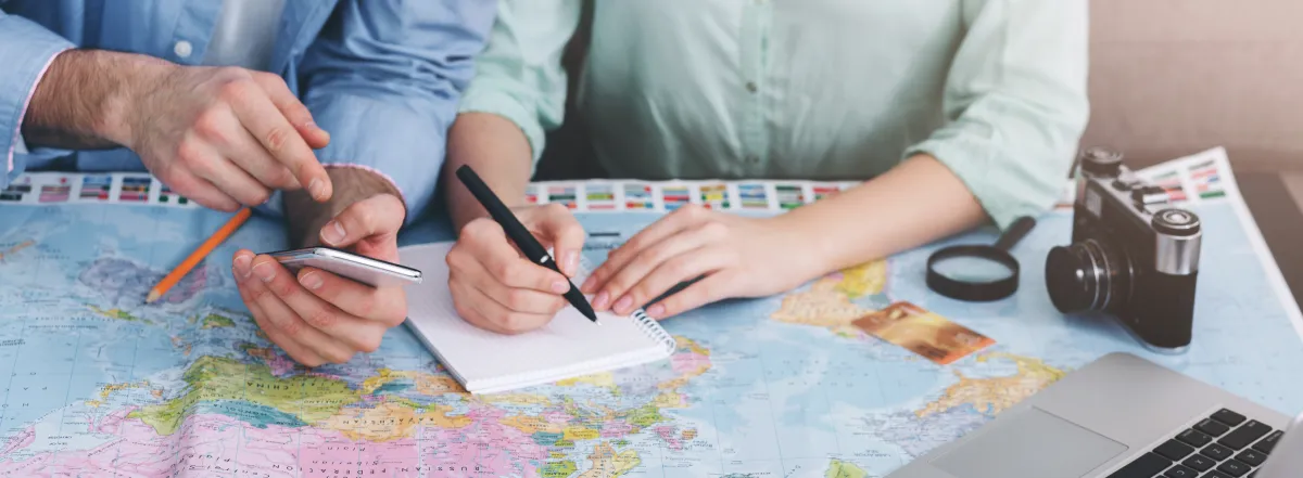 Two people planning vacation with map, notebook and laptop